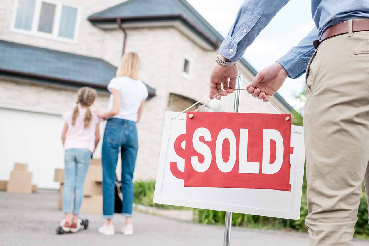 Real estate agent placing a sold sign as a family stands outside their new home, representing a successful home purchase.