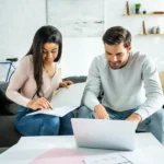 Homebuyers reviewing mortgage pre-approval paperwork on a couch with a laptop