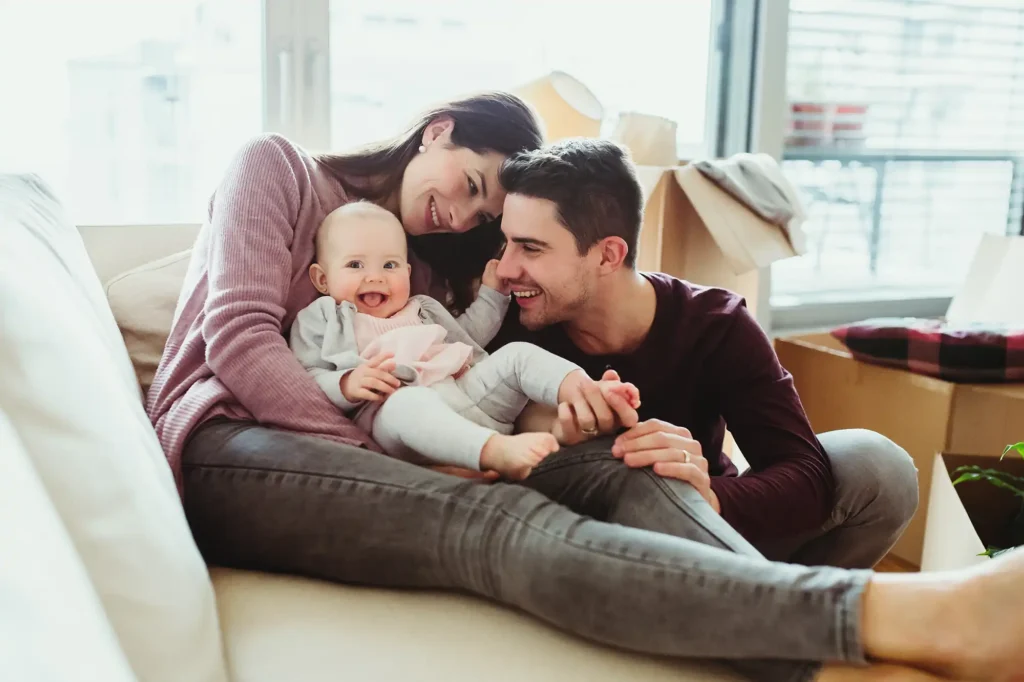 Family with a baby relaxing on a couch in a new home with moving boxes in the background