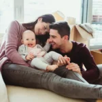 Family with a baby relaxing on a couch in a new home with moving boxes in the background